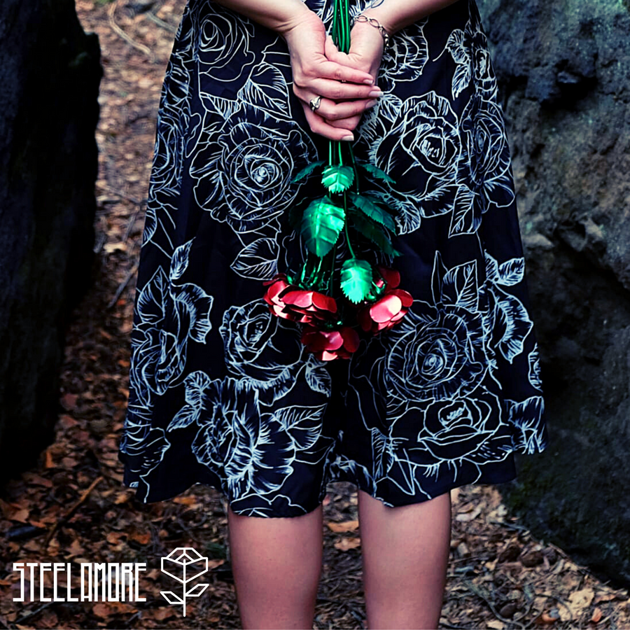 junge Frau mit Rosenstrauß aus edlem Stahl hinter dem Rücken, Blütenblätter rot, Rosenstiel und Rosenblätter grün, fünf rote Rosen aus veredeltem Stahl