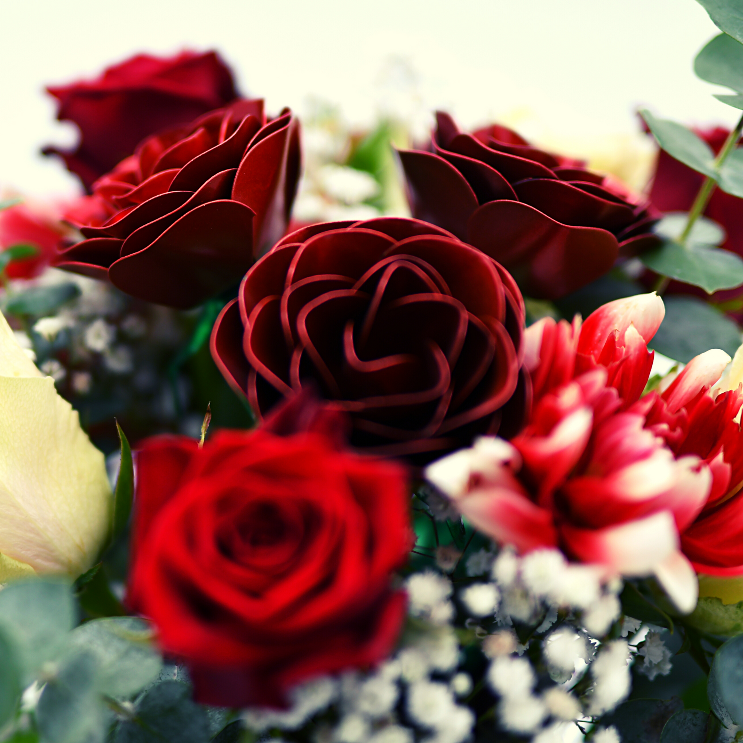 Großaufnahme von einem Strauß roten und weißen Blumen, in der Mitte sind 3 Edelstahlrosen zu sehen, ringsum weiße und rote echte Blumen