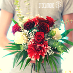 Junger Mann hält einen Strauß mit weißen und roten Rosen in einem grünen Buketin der Hand, die drei Rosen in der Mitte sind Edelstahlrosen, die anderen Blumen sind echte Blumen 